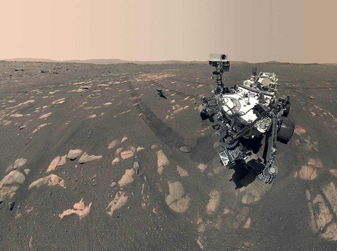 NASA's Perseverance rover photographed by its own arm camera on the surface of Mars, with the Ingenuity helicopter on the ground nearby.