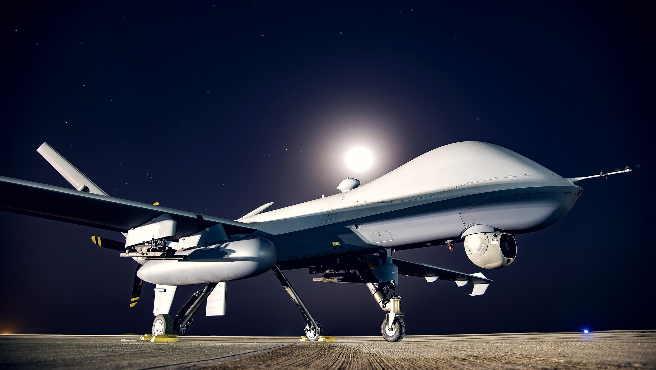 An MQ-9 Reaper unmanned aircraft on a flight line at night, lit under a full moon.