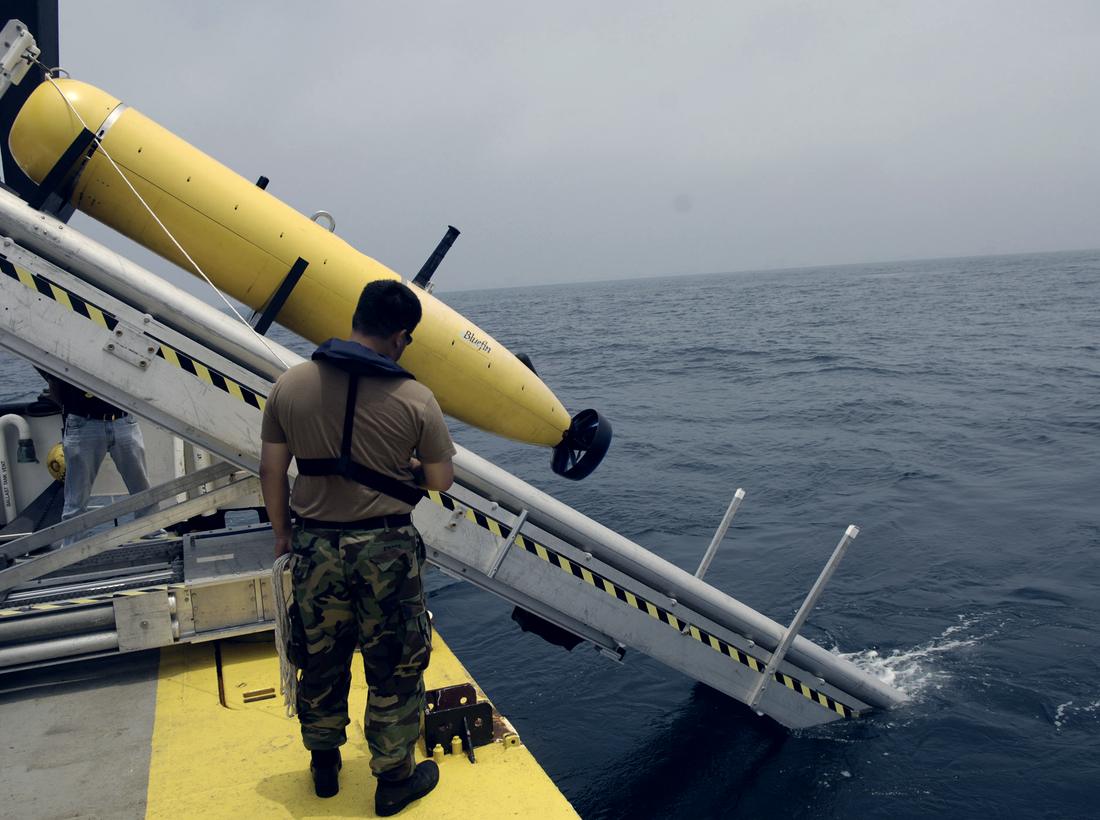 A yellow autonomous underwater vehicle on a launch rail above the water.
