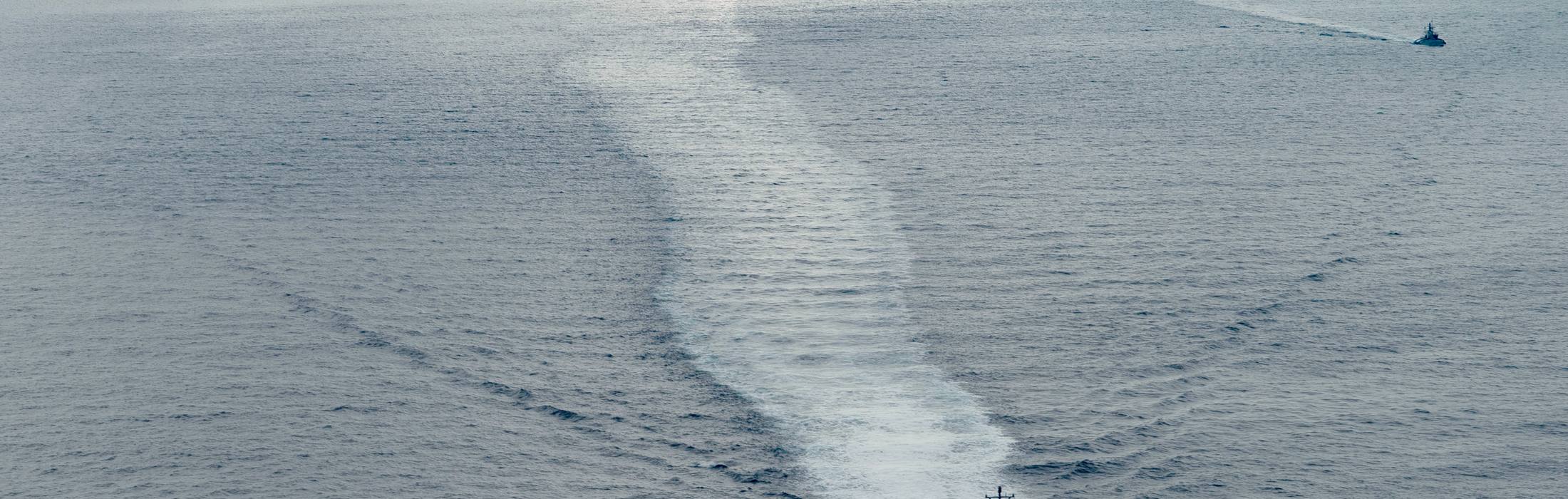 Aerial view of an unmanned surface vessel drawing a long wake across open ocean.